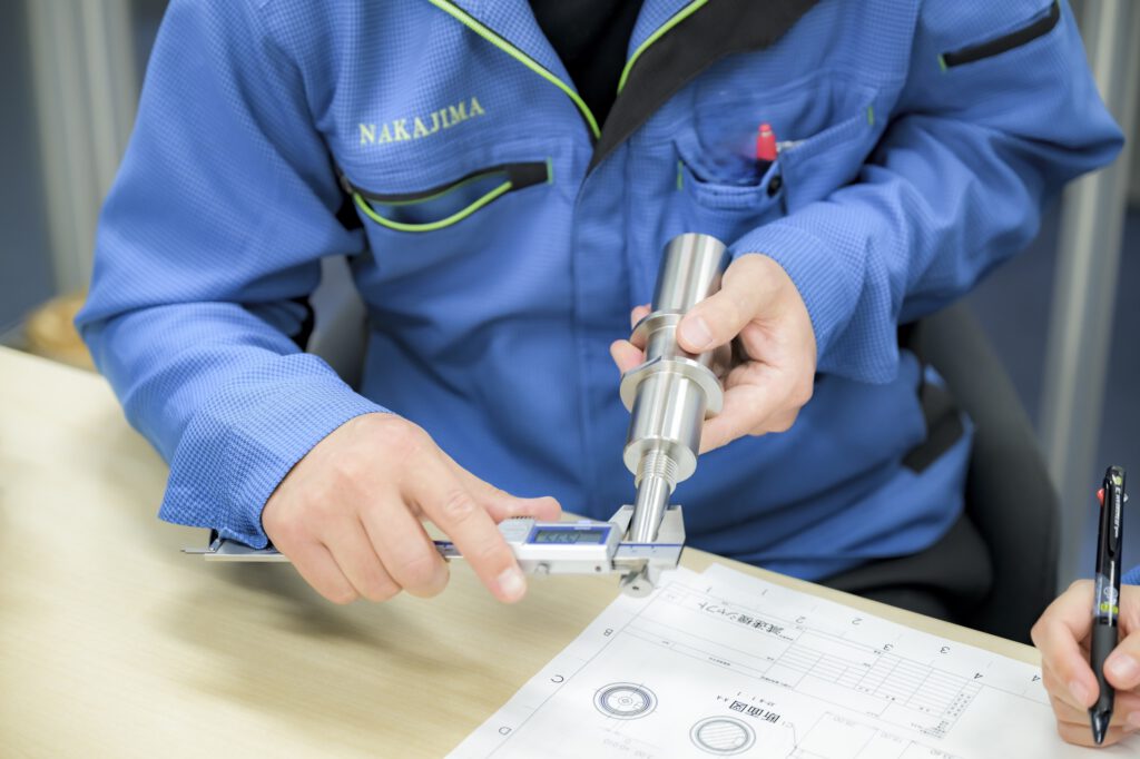 デジタルノギスで加工品の寸法を測定する作業者の手元と図面
